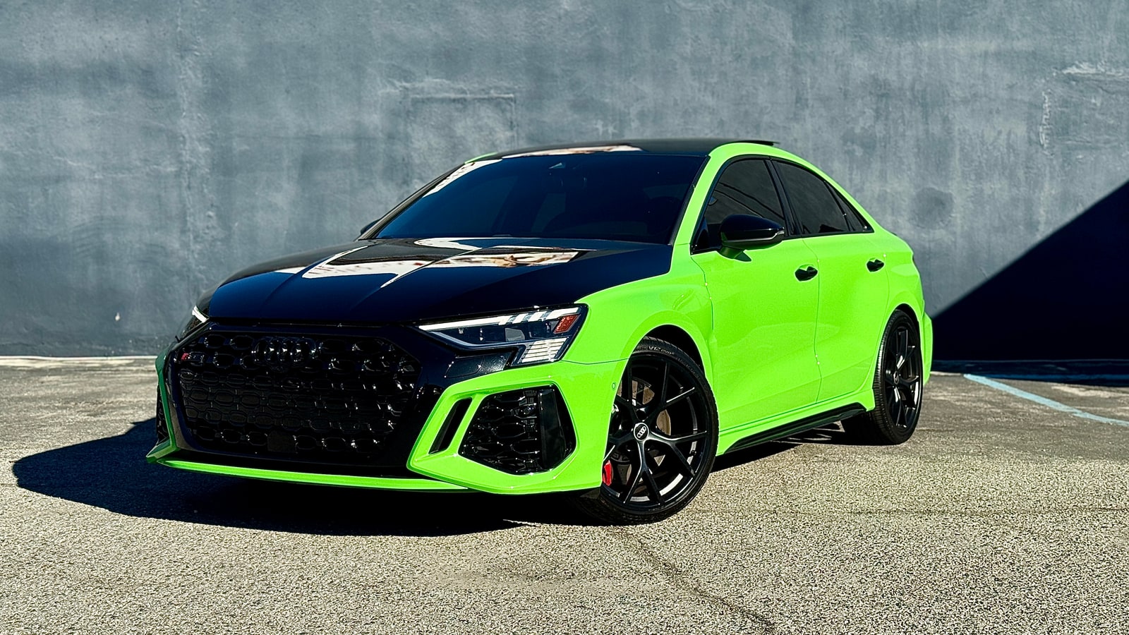 Green Audi RS 3 from a low front three-quarter against a concrete wall