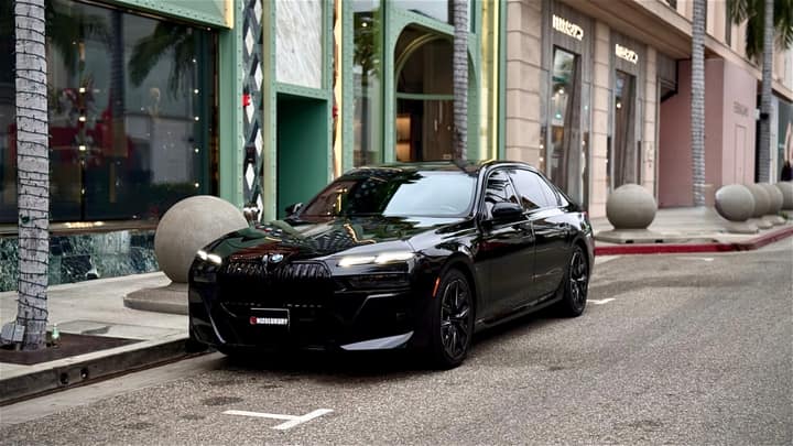 Black BMW 7 Series waiting at the kerb outside a storefront