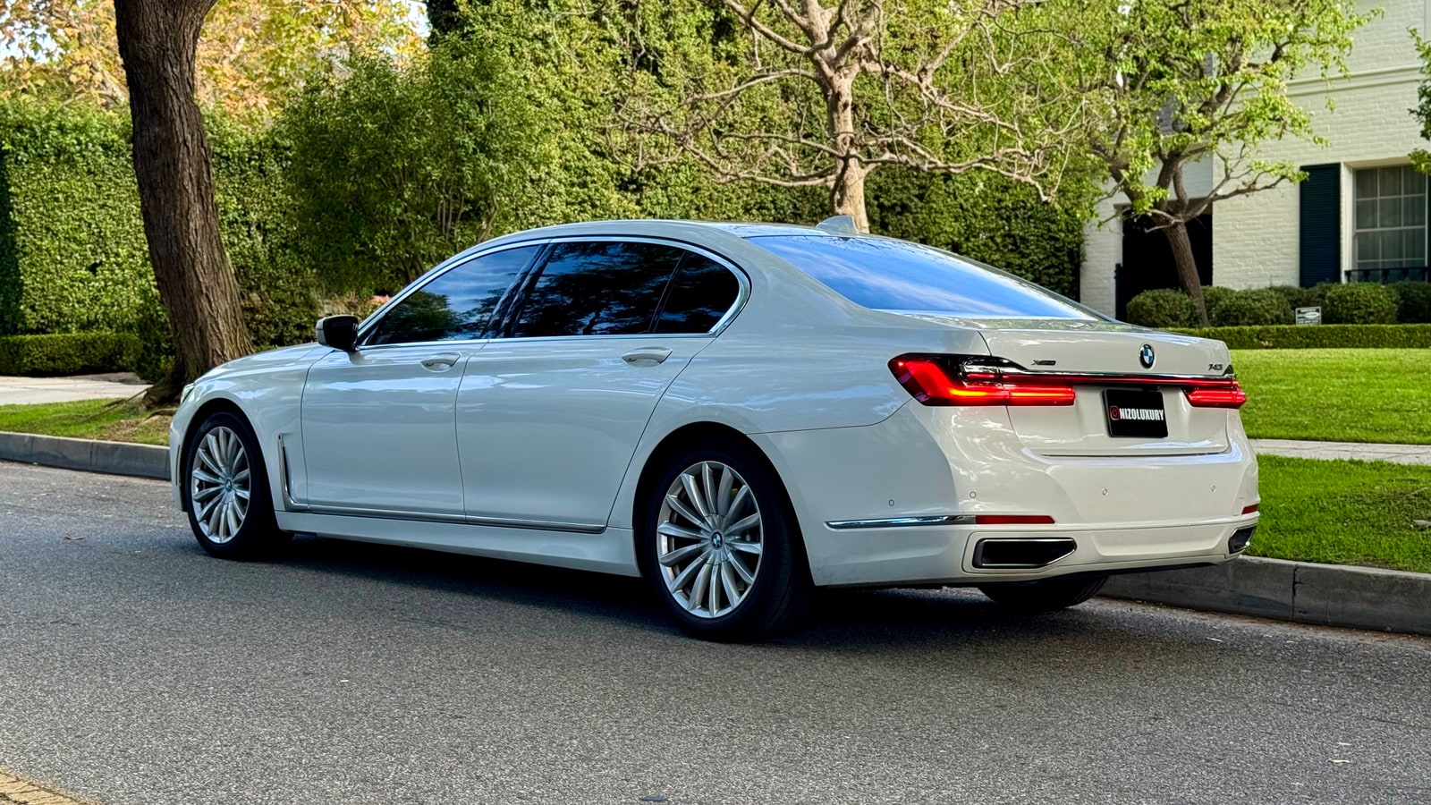 White BMW 7 Series from the rear three-quarter beneath trees