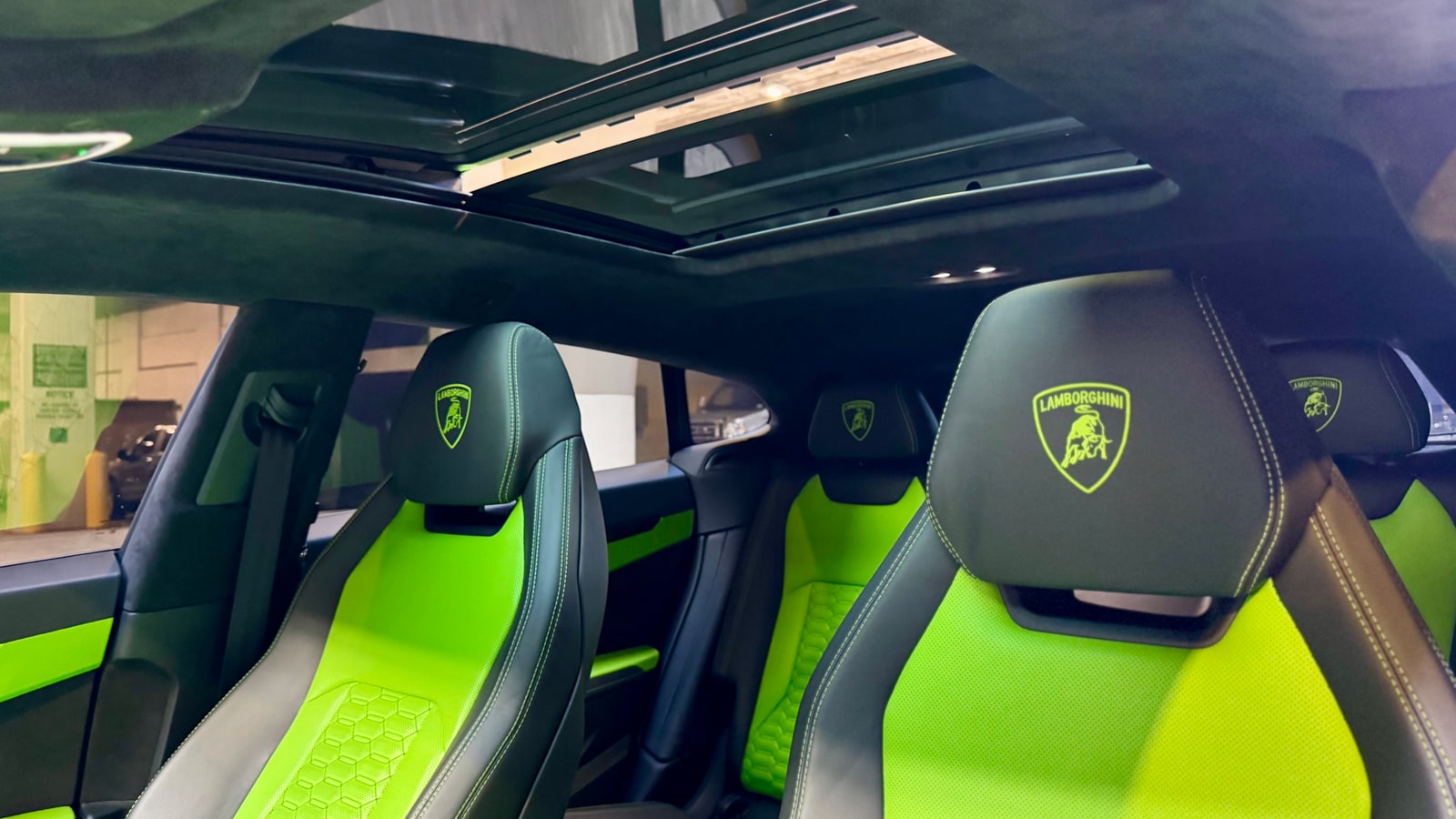 Panoramic roof above green and black seats with the embroidered Lamborghini crest