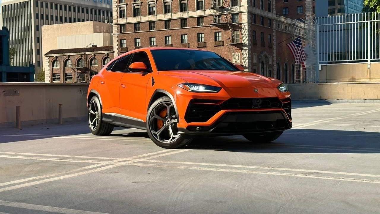 Orange Lamborghini Urus from the right front three-quarter with brick buildings behind