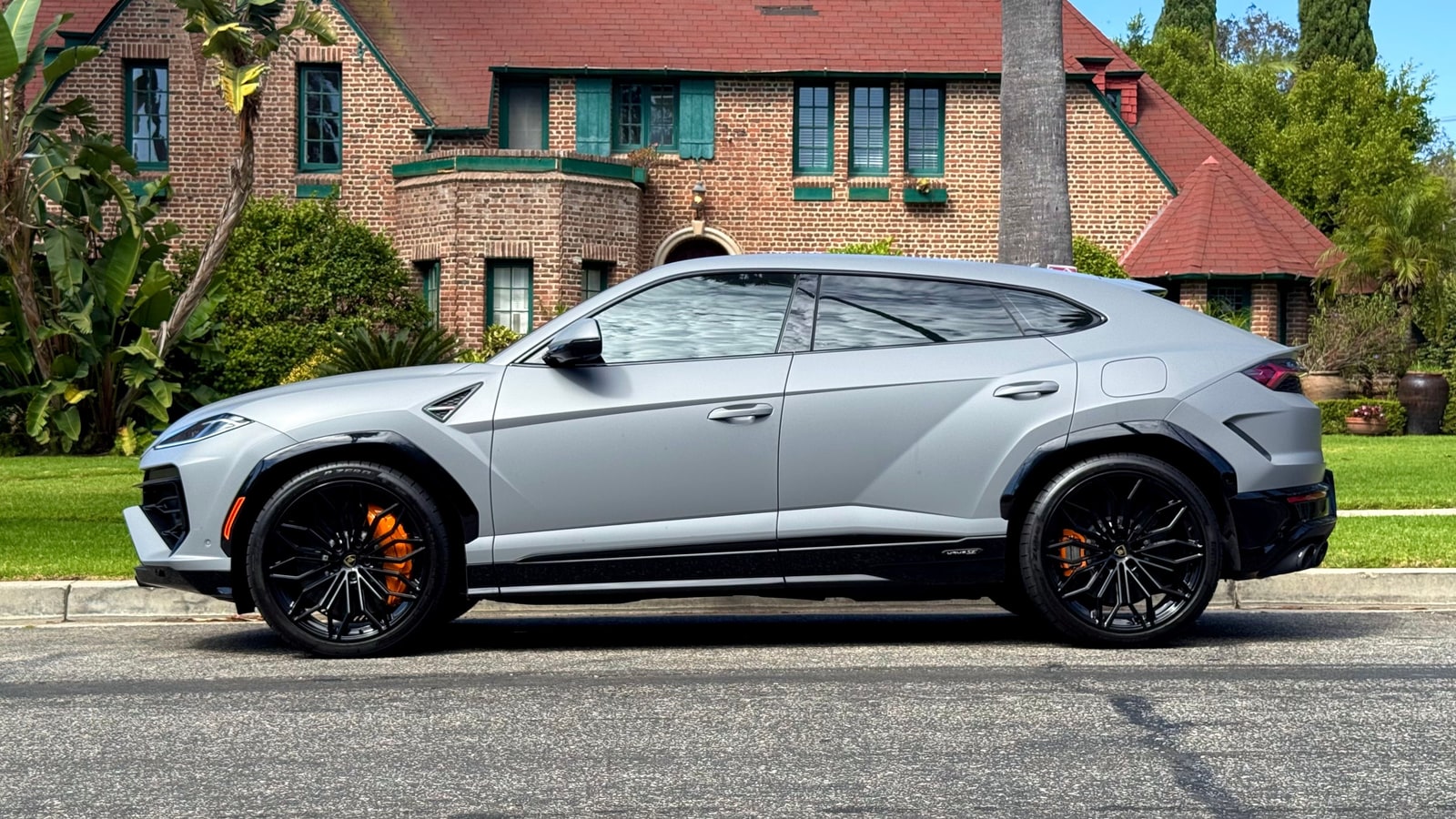 Lamborghini Urus SE in profile outside a brick house, showing the long roofline and black wheels