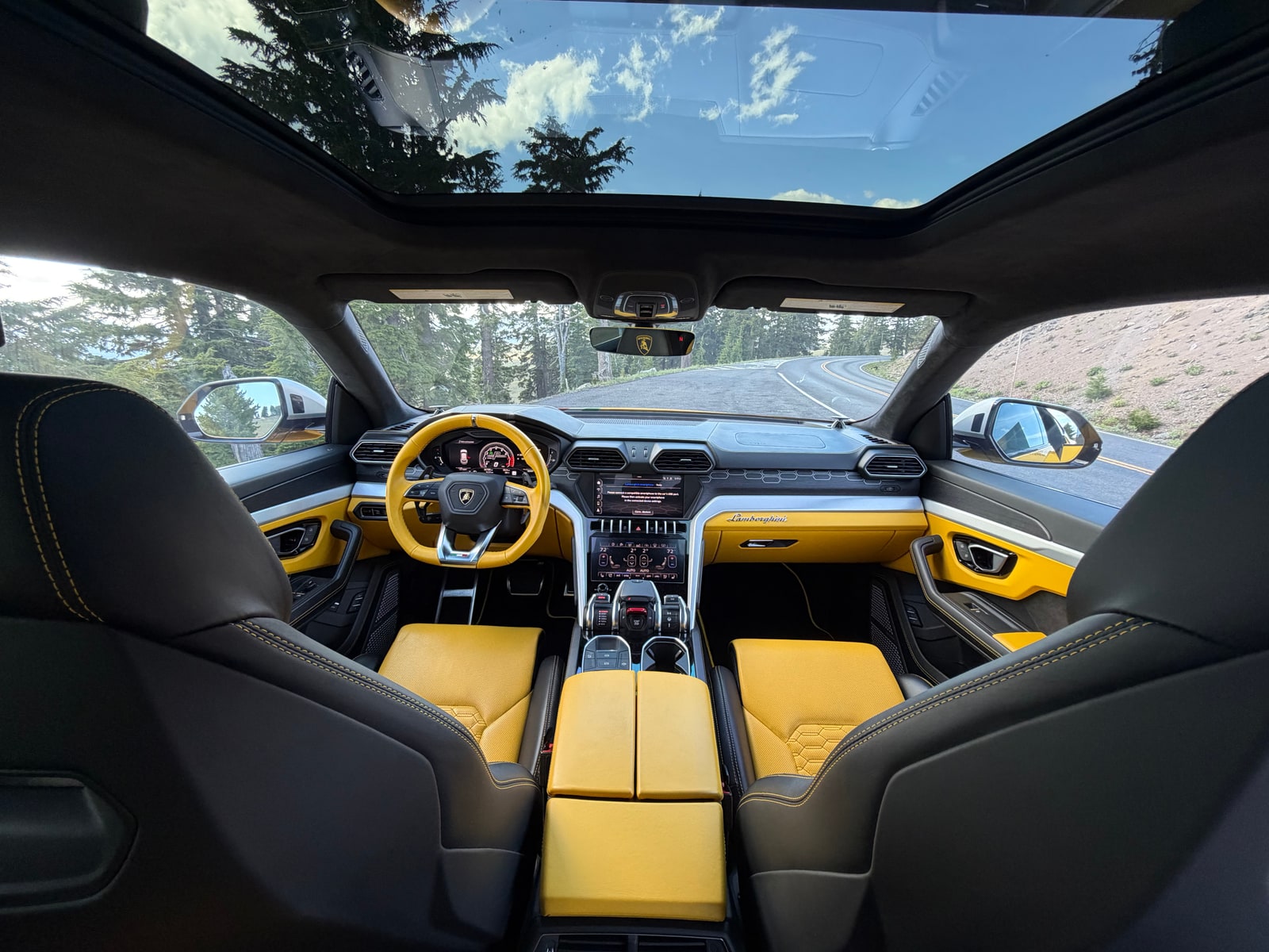 Cabin of the yellow Lamborghini Urus under the panoramic roof, road ahead through the screen
