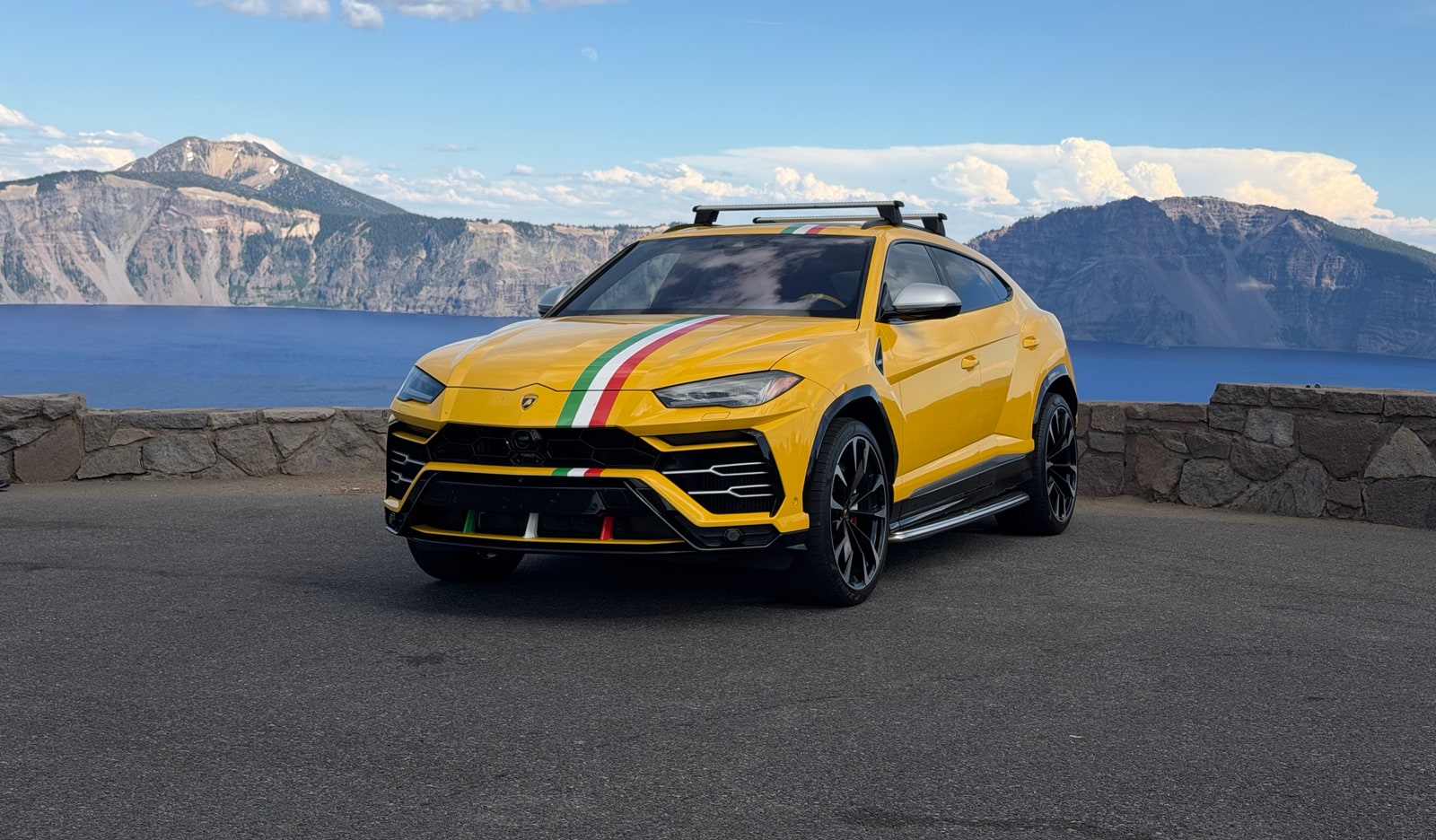 Yellow Lamborghini Urus at a mountain overlook above a lake, Italian tricolour over the bonnet