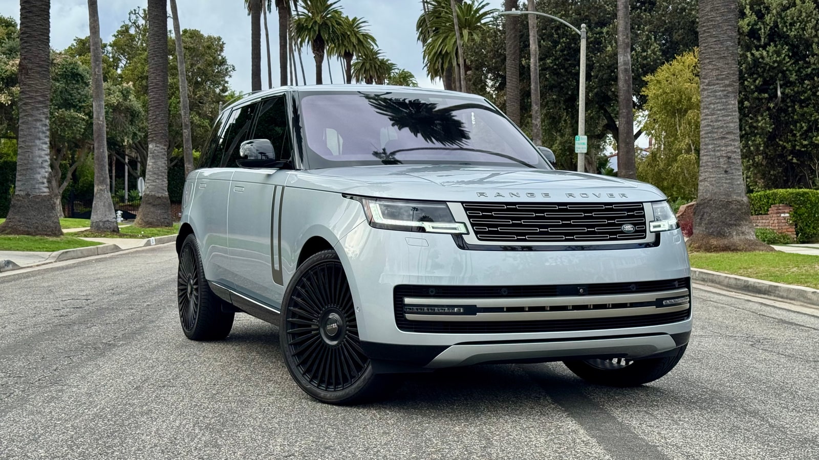 Light silver Range Rover P530 SE from a front three-quarter on a palm-lined Beverly Hills street