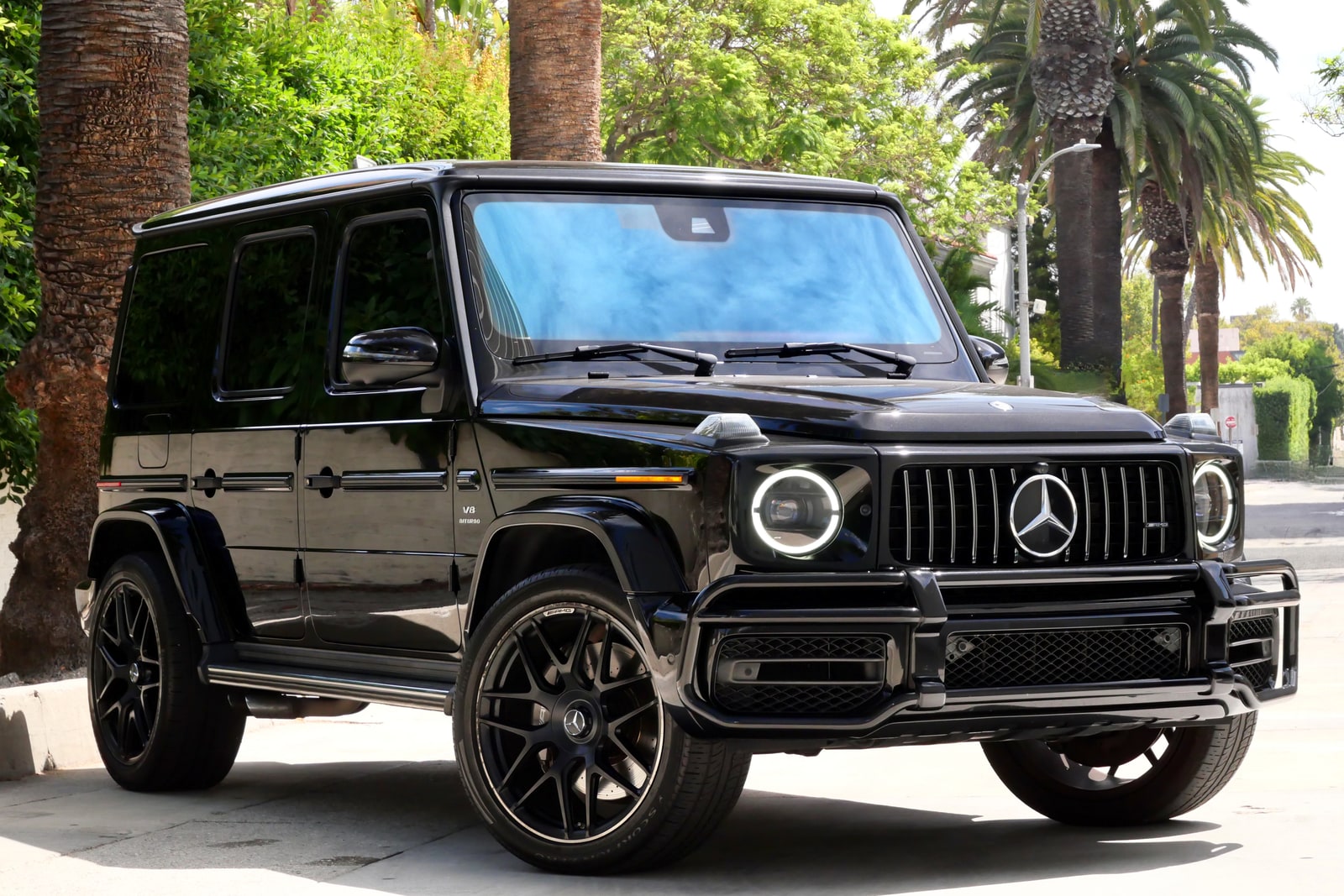 Black Mercedes-AMG G 63 from a low front three-quarter beneath palm trees