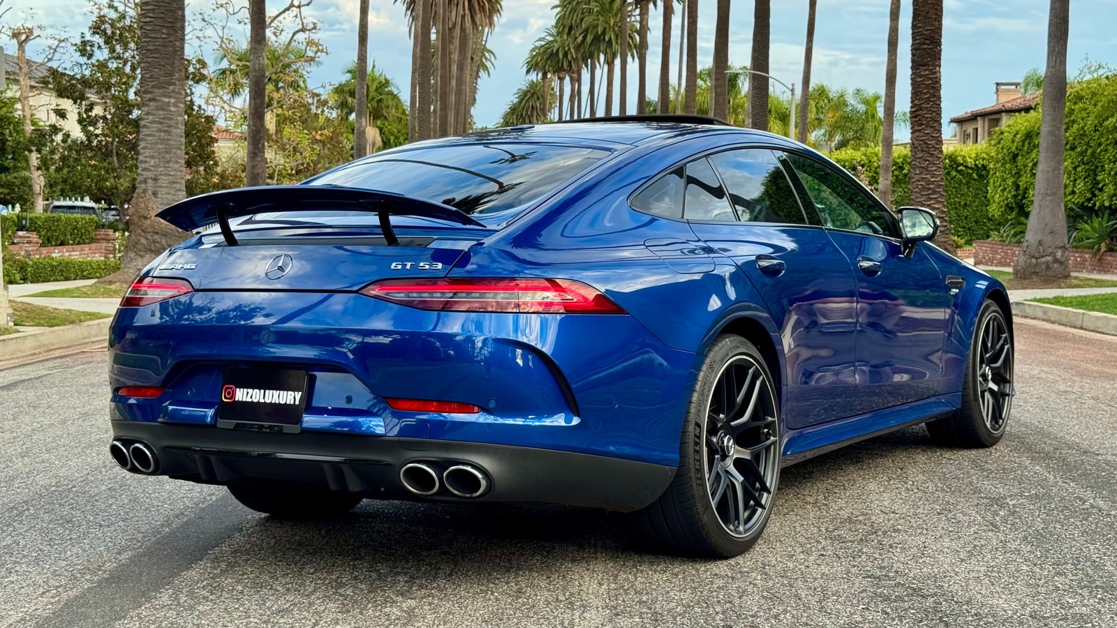 Blue Mercedes-AMG GT 53 from the rear three-quarter showing the fixed wing and quad exhausts