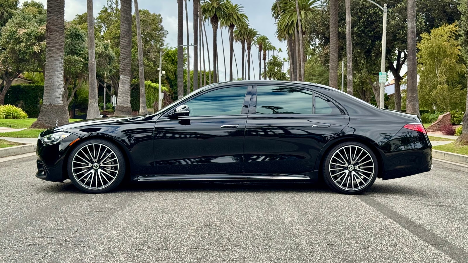 Black Mercedes-Benz S 580 in profile on a residential street with palm trees