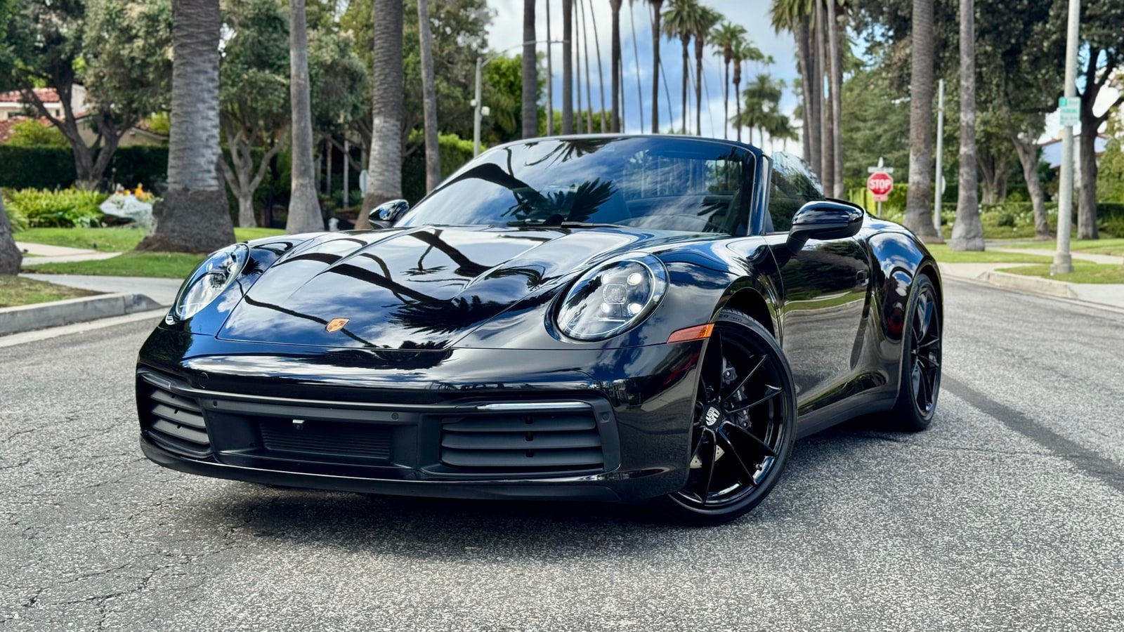 Black Porsche 911 Carrera Cabriolet from a front three-quarter on a palm-lined Beverly Hills street