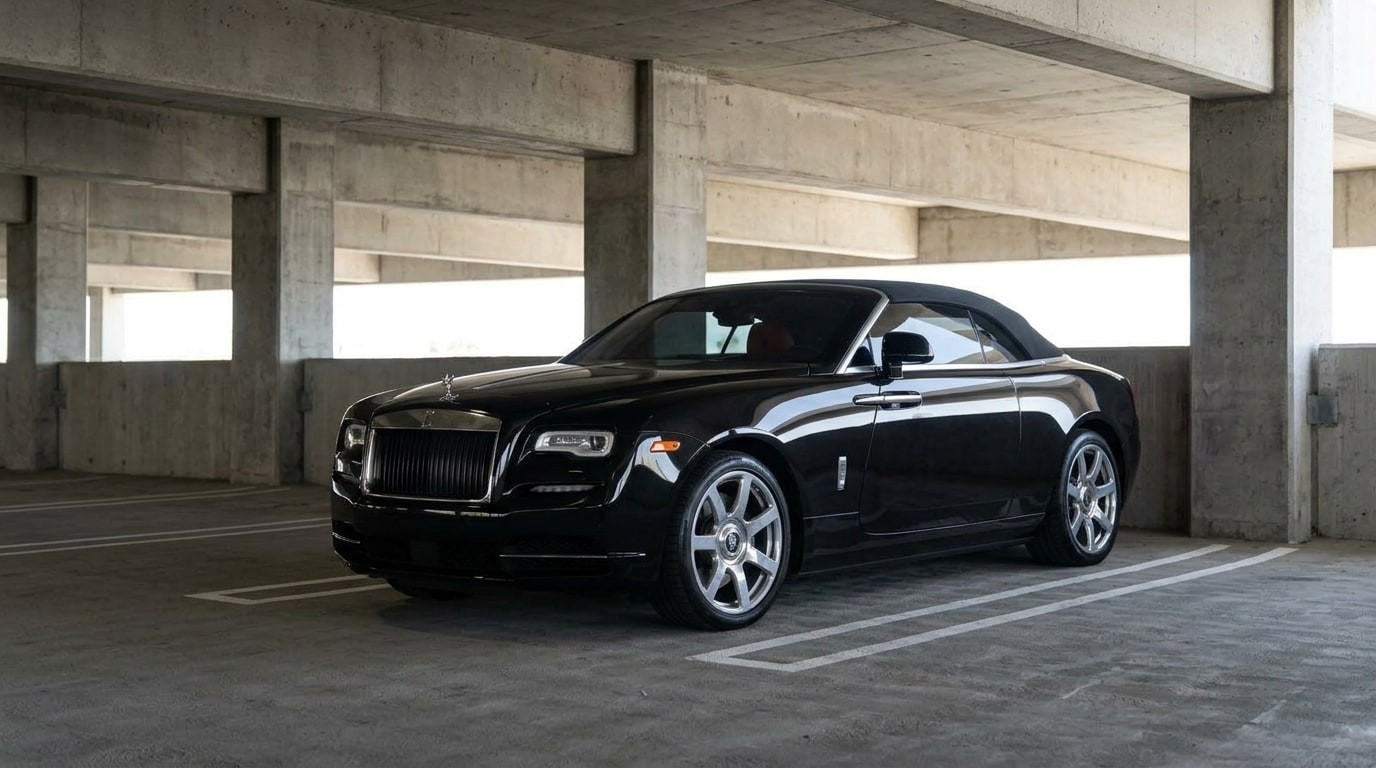 Black Rolls-Royce Dawn convertible with its roof up parked in a bay inside a concrete airport parking structure