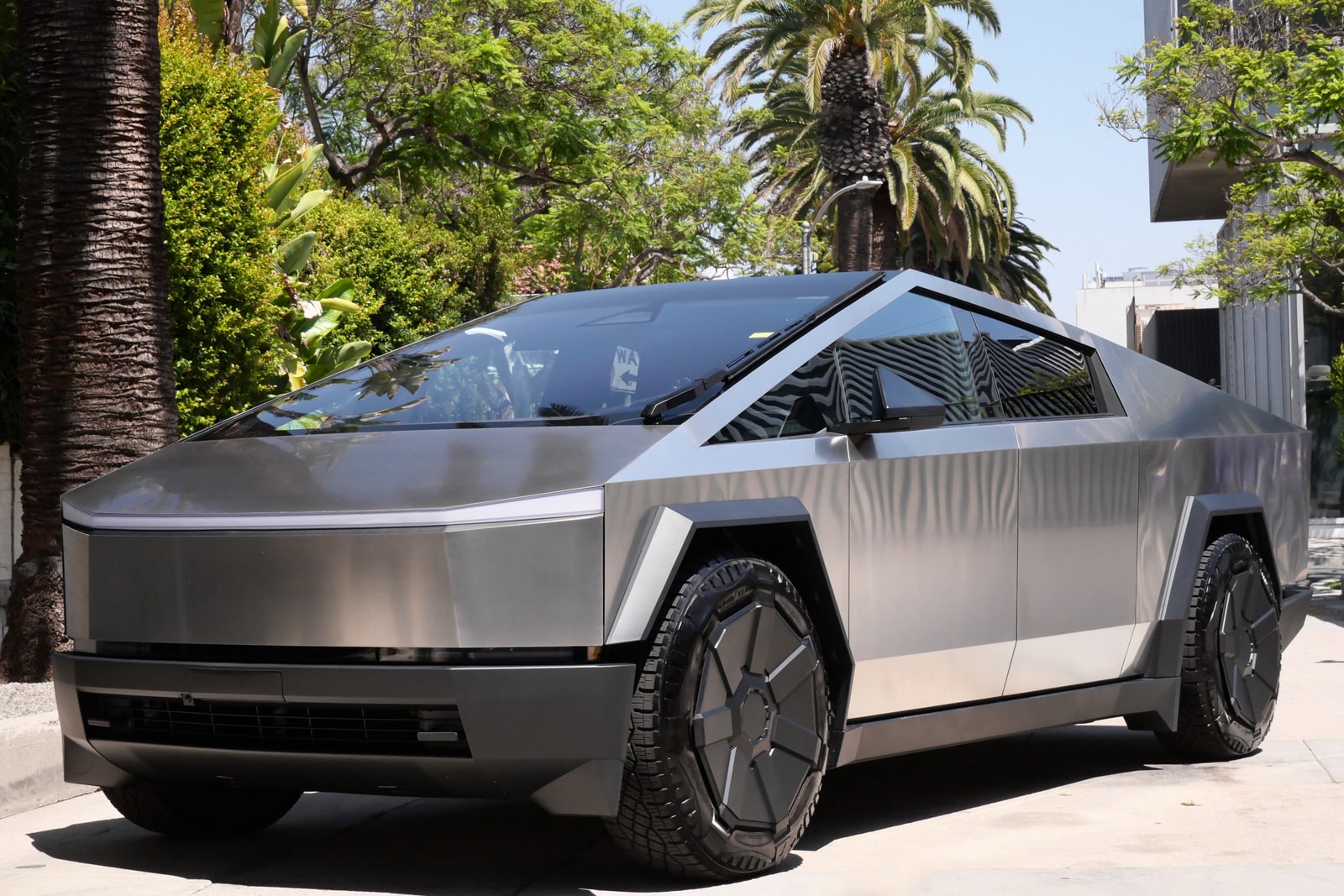 Tesla Cybertruck from a front three-quarter showing the wedge of the windscreen and bare stainless flank